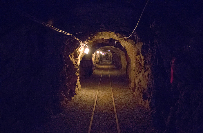 A view into a deep mining tunnel with tracks running down the middle.