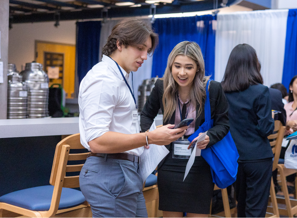 Male and female student look at cell phone at Career Day