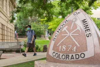 Masked student walks past Mines triangle statue