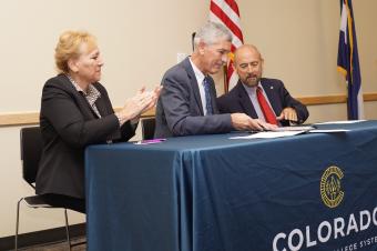 Paul Johnson, center, signs agreement with Joe Garcia and Angie Paccione