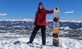 Alaina standing with her snowboard on snowy mountain peak