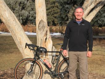 Jeff Gillow stands with bicycle under tree