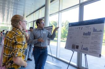 Student talks about research poster to fellow student