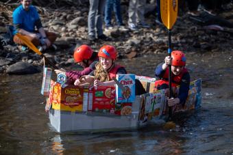 Students paddle down creek in cardboard boat