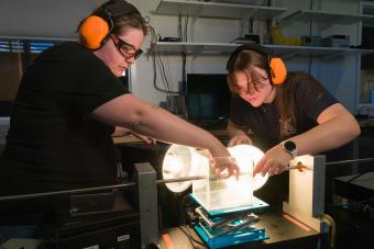 Two students in orange hearing protection perform experiment