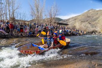 students in cardboard boat floating down creek with mount zion in background