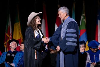 Female graduate wearing cowboy hat shakes hand of President Johnson