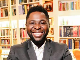 portrait of john akinboyewa in front of book shelves