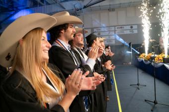 students wearing cowboy hats and graduation gowns clap