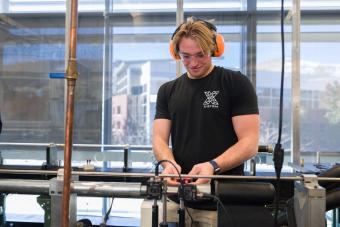 male student wearing black tshirt and orange ear protection working in lab