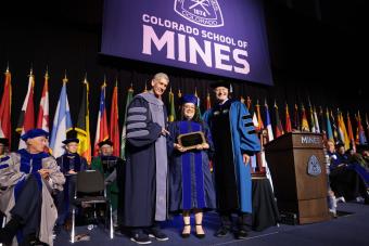 female PhD graduate in regalia holds award between President Johnson and Vice President of Research Walt Copan