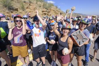 group of students wearing hard hats and holding rocks on mountain