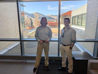 Mark Deinert and Andy Osborne stand in front of window with Mines campus behind