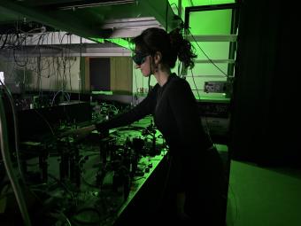 female student in all black working in lab lit by green light