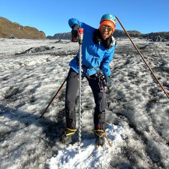 female student standing on glacier drilling into ice