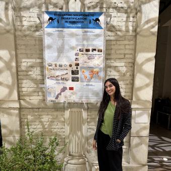 student standing in front of research poster on brick wall