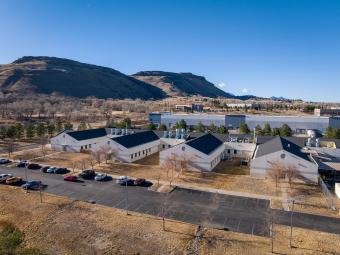 aerial photo of white building with dark roof and four wings and mountains in background