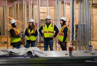 Four construction engineering students in safety vests stand within a construction site