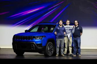 three men holding Mines pennant stand in front of blue Jeep Cherokee