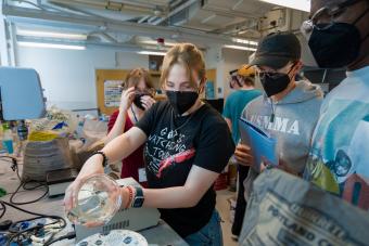 four students wearing masks pour water in concrete mix in lab