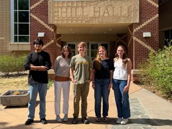 group photo of five students standing in front of hill hall
