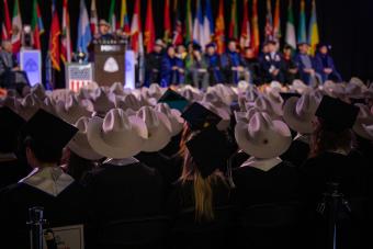 graduates in a mix of cowboy hats and mortarboards sit in front of commencement stage