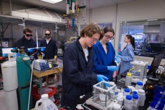 four students in lab coats work at various stations in a lab