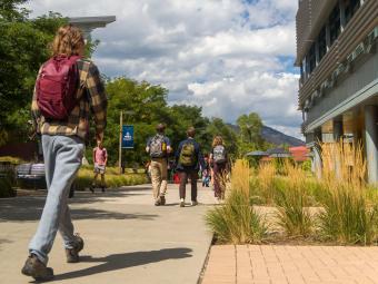 student wearing backpack walks down pedestrian sidewalk with more students walking ahead