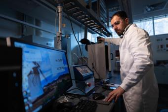 researcher in white lab coat in front of computer monitor with figures on the screen