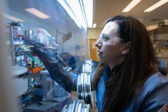jen shafer in blue lab coat and safety glasses working in a laboratory glove box
