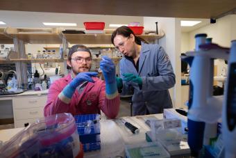 jen shafer in blue lab coat and student in pink lab coat look at a specimen in the lab