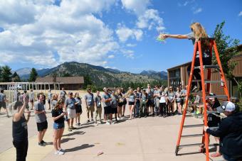 Student at top of orange ladder prepares to drop an egg inside a bundle of colored straws