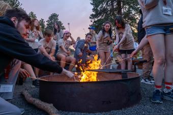 Mines students at Oredigger Camp stand around a fire pit roasting marshmellows