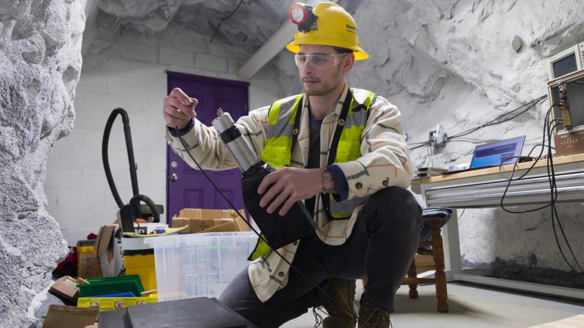 PhD student in safety gear in an underground mine chamber working on a scintillator