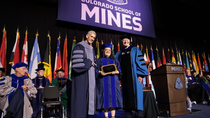 female PhD graduate in regalia holds award between President Johnson and Vice President of Research Walt Copan