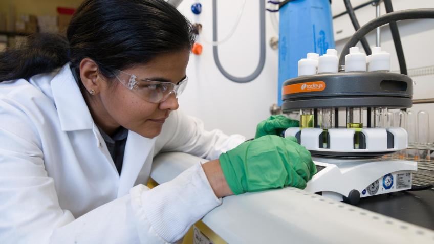 ramya kumar in lab coat and green gloves working in lab