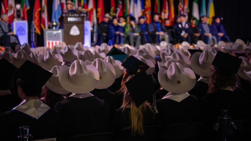 graduates in a mix of cowboy hats and mortarboards sit in front of commencement stage