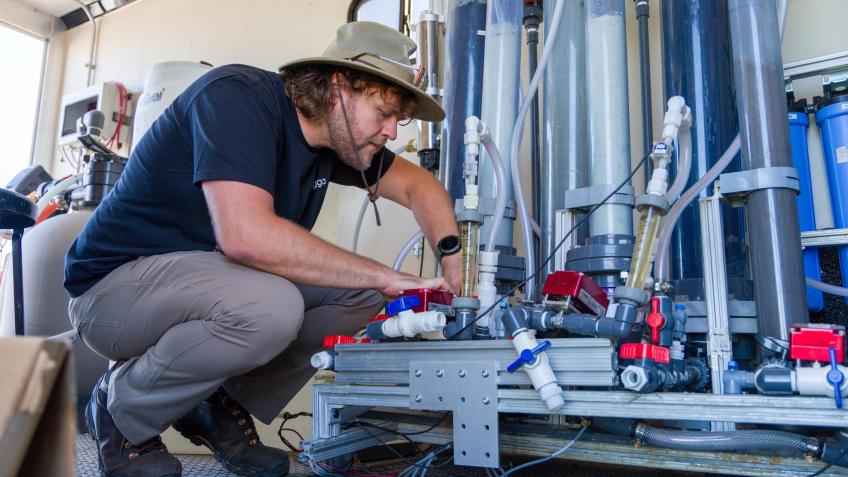 male researcher in hat works on pfas treatment system inside a trailer