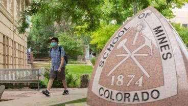 Masked student walks past Mines triangle statue