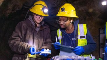 Two students in hardhats look at sample in mine