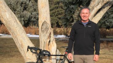 Jeff Gillow stands with bicycle under tree