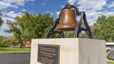 Sesquicentennial bell in front of blue sky and green trees