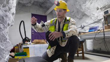 PhD student in safety gear in an underground mine chamber working on a scintillator