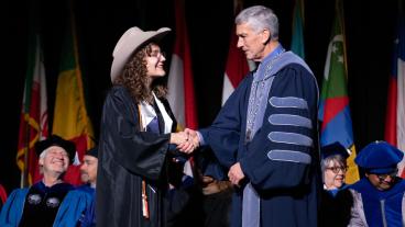 Female graduate wearing cowboy hat shakes hand of President Johnson