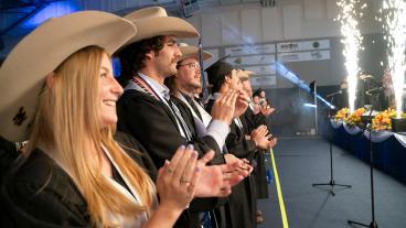 students wearing cowboy hats and graduation gowns clap