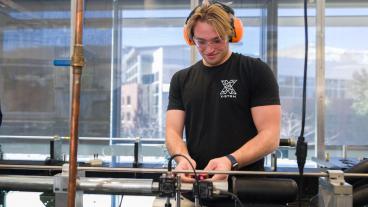 male student wearing black tshirt and orange ear protection working in lab