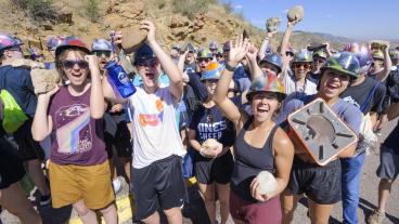 group of students wearing hard hats and holding rocks on mountain