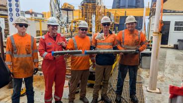 five people in safety orange hold drill core aboard boat