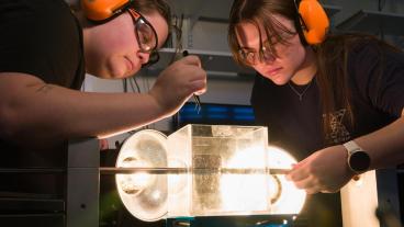 two female students wearing orange ear muffs conducting experiment in lab