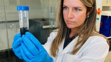 lori tunstall in white lab coat and blue gloves holding a test tube